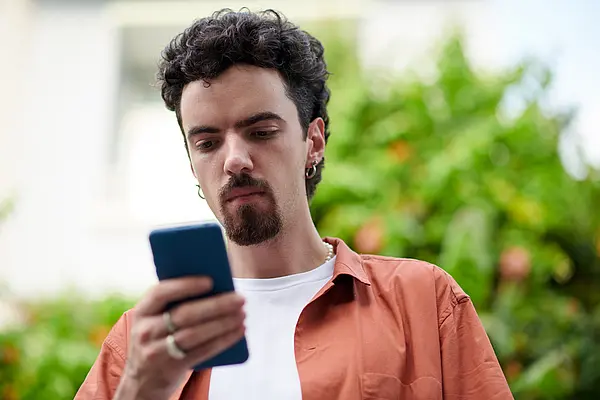 Mann mit Bart schaut draußen auf sein Smartphone. Hintergrund leicht verschwommen.